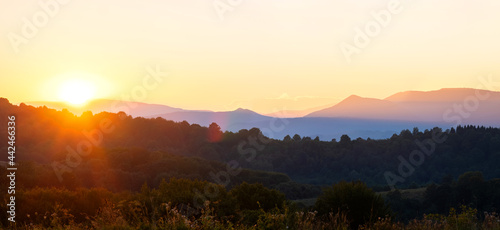 Beautiful panoramic mountain landscape with hazy peaks and foggy valley at sunset.
