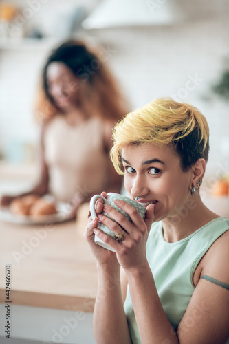 Cheerful woman drinking coffee and friend at distance