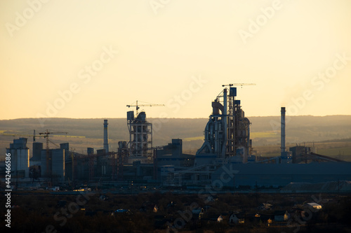 High concrete structure of cement factory with tower crane and smoking chimney. Industrial production and air pollution concept.