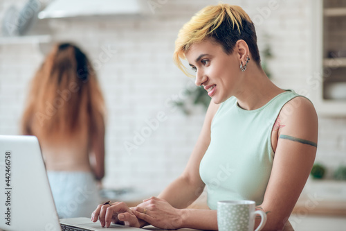 Smiling woman behind laptop and girlfriend back photo