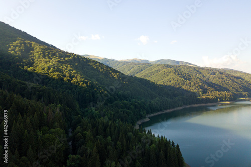 Aerial view of big lake with clear blue water between high mountain hills covered with dense evergreen forest.