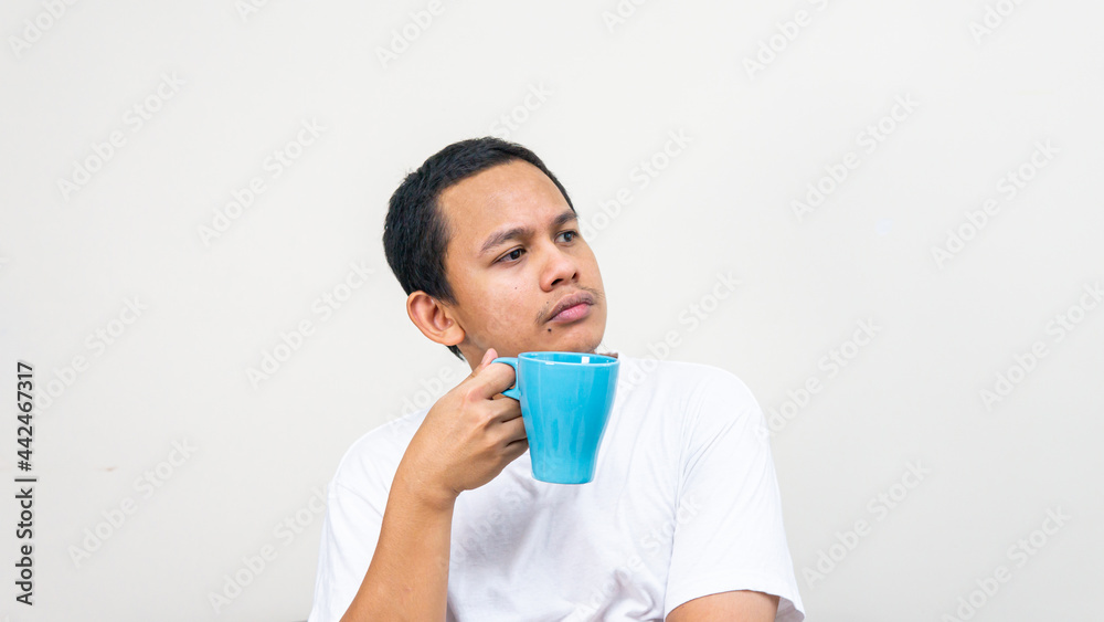 A portrait of Asian Malay man day dreaming and thinking on something with the blue tea cup on his hand. A portrait of Asian Malay man day dreaming and thinking on something with the blue tea cup on his hand.