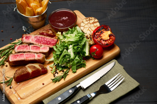 Grilled sliced roated beef steaks, potato and sauce on wooden cutting board photo