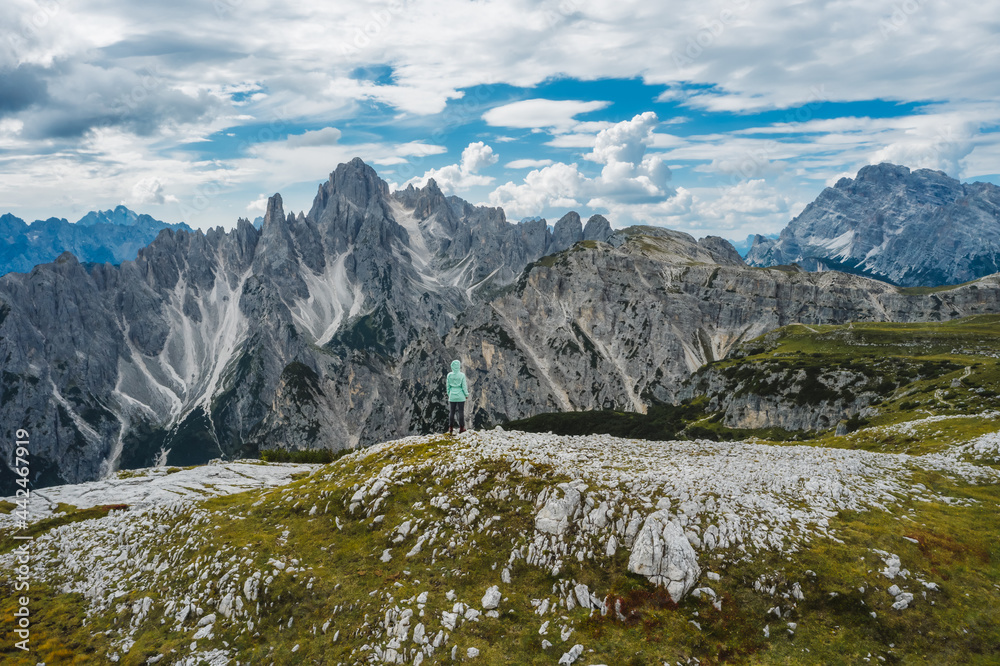 Aerial view of a woman hiker in green jacket against Cadini di Misurina mountain peaks in background. Italian Alps, Dolomites, Italy, Europe