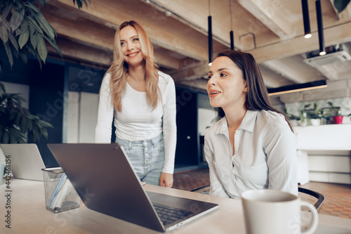 Two young female colleagues discussing business project together in office