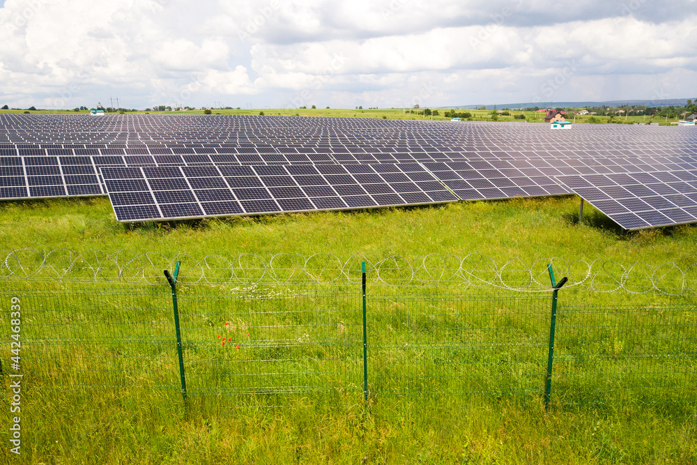 Aerial view of solar power plant on green field with protective wire fence around it. Electric panels for producing clean ecologic energy. Aerial view of solar power plant on green field with protective wire fence around it. Electric panels for producing clean ecologic energy.