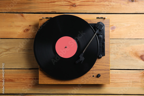 Modern vinyl record player with disc on wooden background, top view