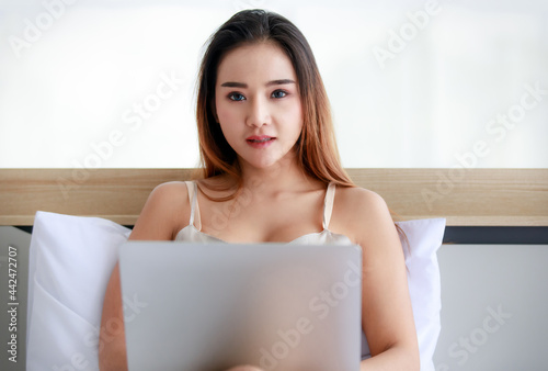 Young Asian female with laptop resting on bed
