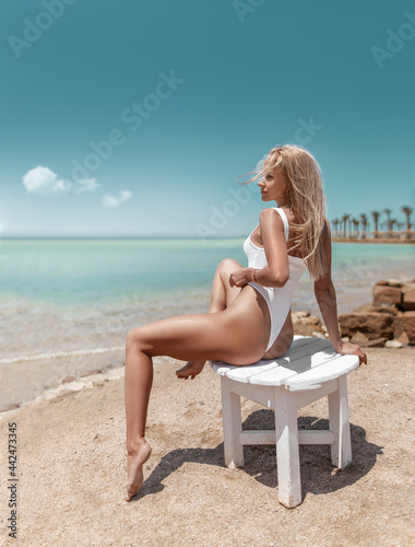 Obraz na plátně Beautiful fitness woman with perfect butt and legs in white swimwear posing on the ocean beach shore