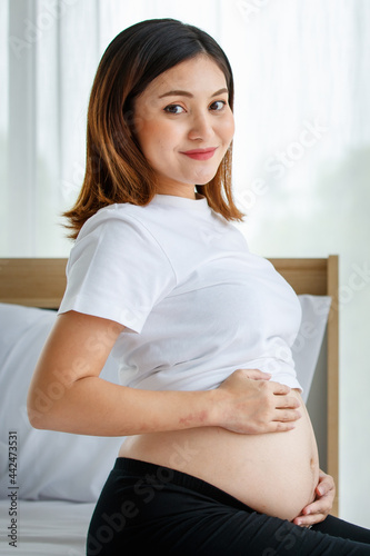 happy smiling young beautiful Asian pregnant woman sitting on a bed looking and touching her belly with care and love. Expecting for a strong and healthy baby Free Download happy smiling young beautiful Asian pregnant woman sitting on a bed looking and touching her belly with care and love. Expecting for a strong and healthy baby - GFXLoad