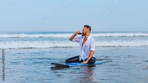 .European man drinking wine while sitting on a surfboard.