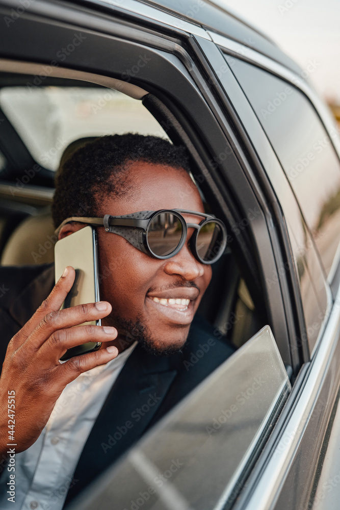 Smiling black businessman with smartphone inside of car