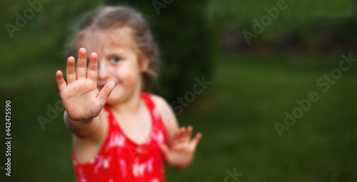 hand of a happy cute little girl in a field in the red dress on green grass background