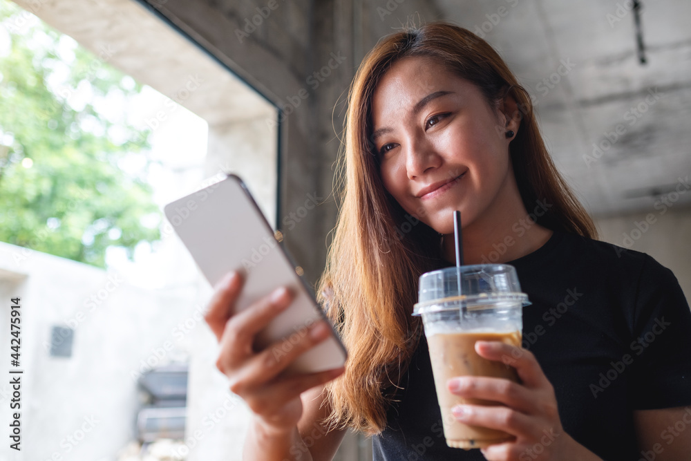 Closeup image of a beautiful young asian woman holding and using mobile phone while drinking coffee in cafe Closeup image of a beautiful young asian woman holding and using mobile phone while drinking coffee in cafe