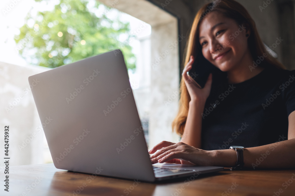 Closeup image of a businesswoman using mobile phone and working on laptop computer in office Closeup image of a businesswoman using mobile phone and working on laptop computer in office
