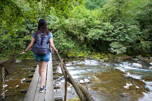 A slender brunette crosses a mountain river on a hinged bridge.