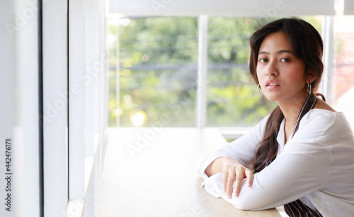 Free Download Serene Asian waitress in uniform sitting at counter in cafe and leaning on hand while looking at camera - GFXLoad