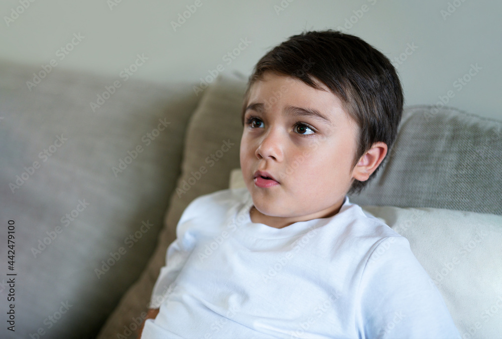 Authentic Kid sitting on sofa watching TV, Emotional portrait Young boy siting on sofa looking out with thinking face or nervous, Children Health care