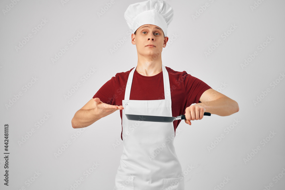 a man in a white apron a frying pan in his hands preparing food for professionals light background a man in a white apron a frying pan in his hands preparing food for professionals light background