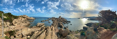 granite rocks shaped by wind and water in front of sky, clouds and light reflections in the water surface on the north coast of sardinia