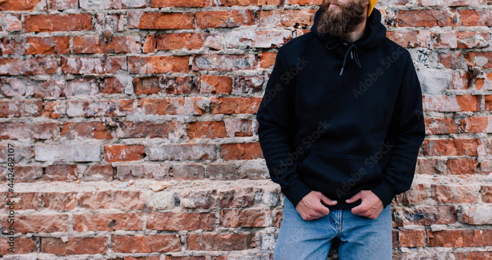 Obraz premium City portrait of handsome guy wearing black blank hoodie and baseball cap with space for your logo or design. Mockup for print