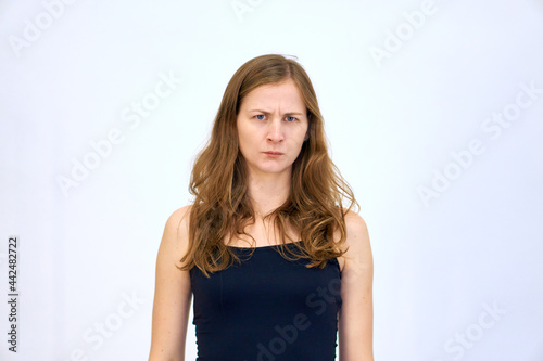Serious emotion and frowning brows. beautiful Caucasian woman stands on a white background in a blue sweater with loose hair. The woman shows emotions. © Vladimir