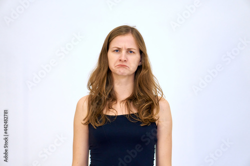 Sadness and drooping lips. beautiful Caucasian woman stands on a white background in a blue sweater with loose hair. The woman shows emotions. © Vladimir