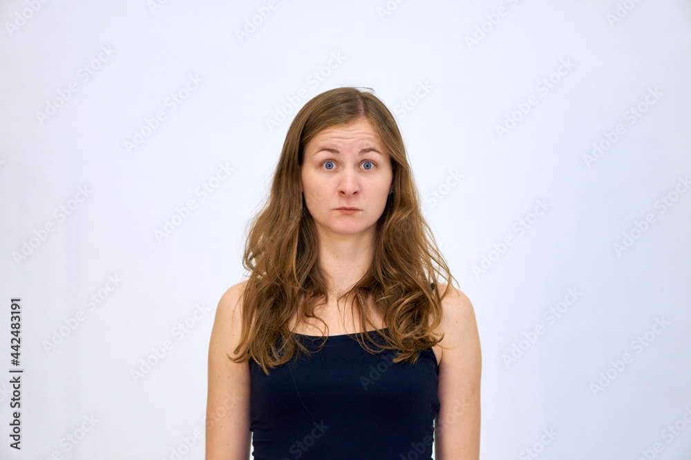 The woman thought for a moment and looks with surprise. A beautiful Caucasian woman stands on a white background in a blue sweater with loose hair. The woman shows emotions.