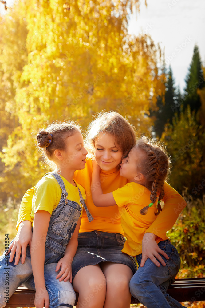 Two young little girl and his mother with blonde hair in an autumn park on a yellow and orange leaf background. Family walking in forest