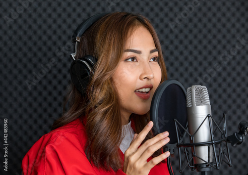 Ethnic female singer in headphones singing in microphone and recording music in studio