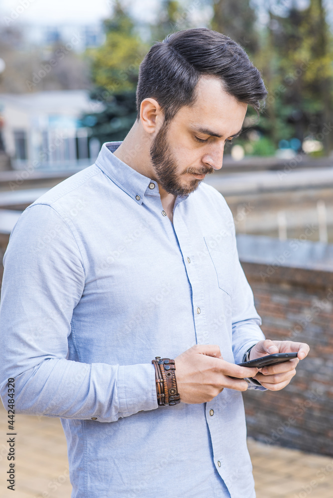 Obraz premium Portrait of a man businessman in a shirt with a beard who stands and uses a smartphone