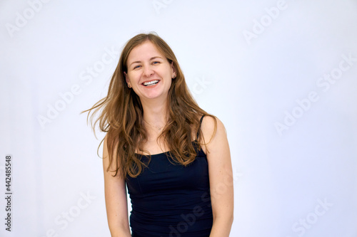 Happy woman smiles and laughs. Joyful emotion. A beautiful Caucasian woman stands on a white background in a blue sweater with loose hair. The woman shows emotions.