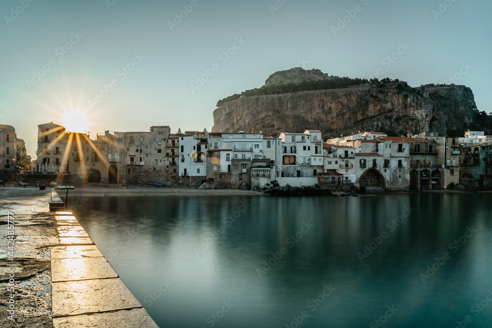 Fototapeta premium Sunrise in harbor of Cefalu, Sicily, Italy, old town panoramic view with colorful waterfront houses, sea and La Rocca cliff.Attractive summer cityscape,traveling concept background.Italian vacation.