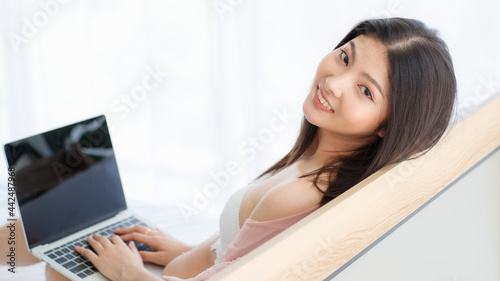 Beautiful young naughty sexy girl on pajamas sit back against bed head enjoy laptop working and happily turn back with lovely smile to look at someone in bright morning of rest day