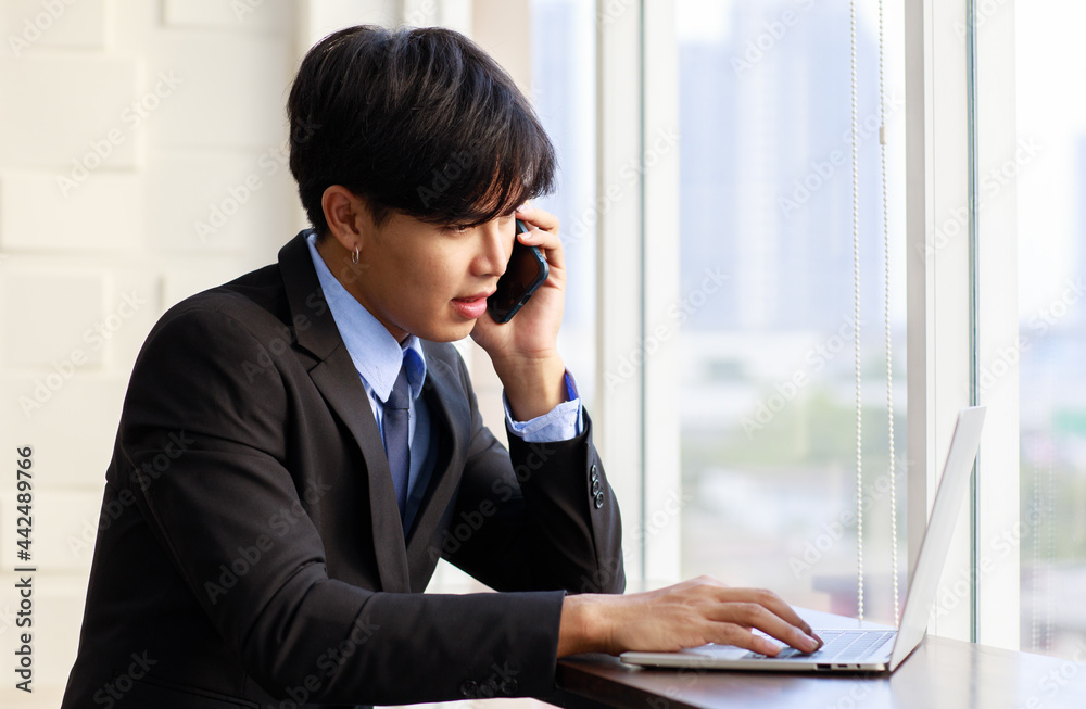 Portrait one young asian businessman are smart and handsome wearing black suit sitting chair talking phone while feel confident with smiling as smile on face looking at camera with laptop Portrait one young asian businessman are smart and handsome wearing black suit sitting chair talking phone while feel confident with smiling as smile on face looking at camera with laptop