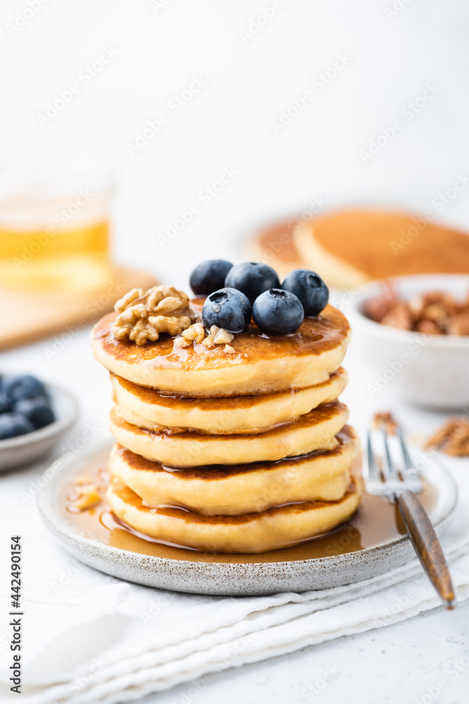 Stack of pancakes served with maple syrup, blueberries and walnuts on a plate, closeup view, white background Stack of pancakes served with maple syrup, blueberries and walnuts on a plate, closeup view, white background
