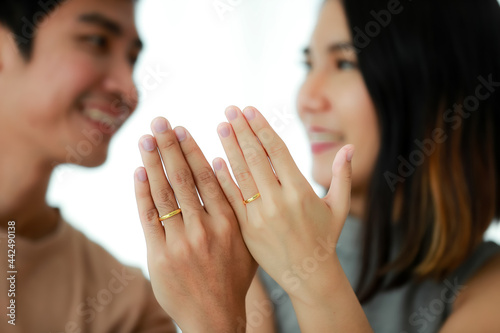 Portrait shot of cute smiling young Asian lover couple showing a golden wedding rings that wore in their fingers. Selective focus at the rings in white background