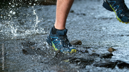 Freeze motion of legs of a runner in sneakers splashng in forest stream. Close-up.