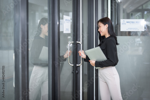Young businesswoman with laptop opening meeting room door.