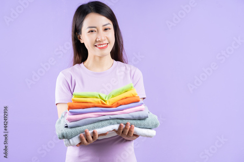 Young Asian woman holding a stack of clothes on purple background