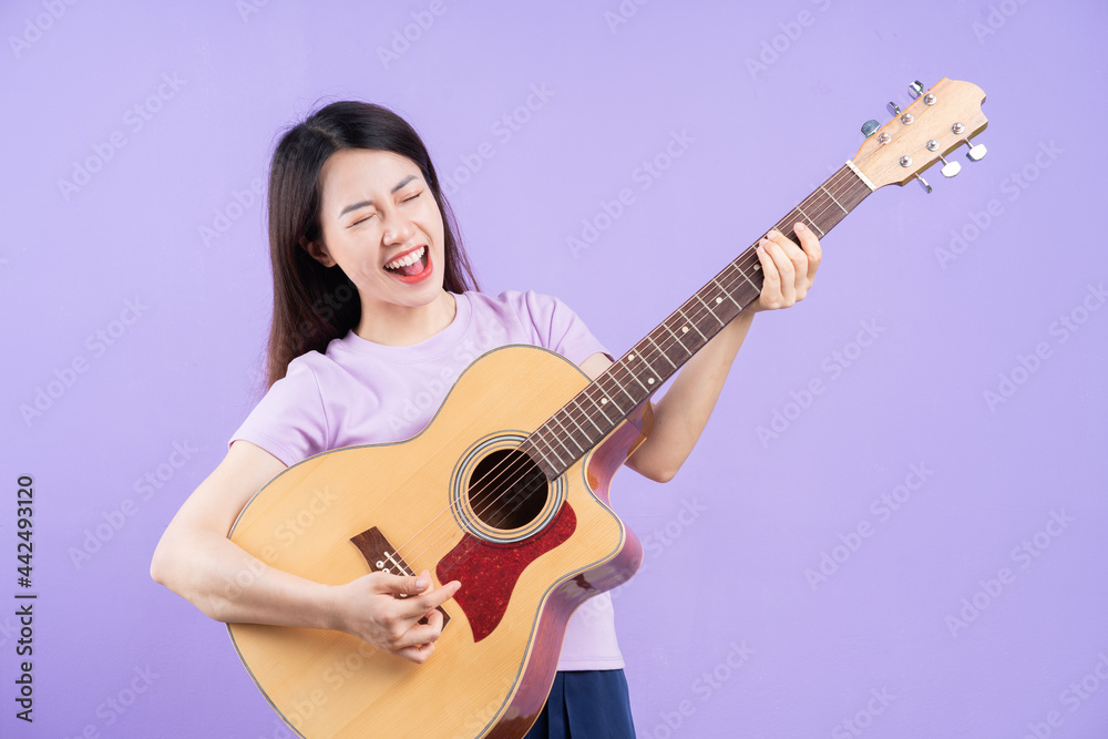 Young Asian woman playing guitar on purple background Young Asian woman playing guitar on purple background