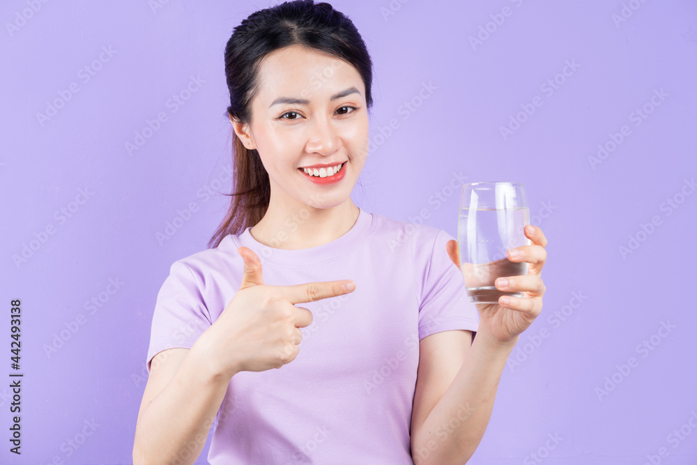 Young Asian woman holding glass of water on purple background Young Asian woman holding glass of water on purple background