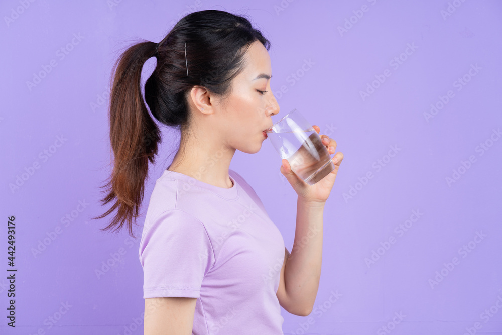 Young Asian woman holding glass of water on purple background Young Asian woman holding glass of water on purple background
