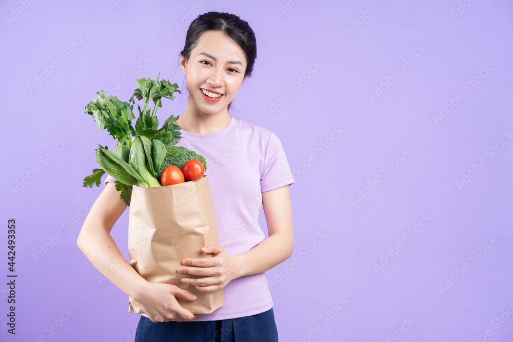 Young Asian woman holding a bag of vegetables on purple background Young Asian woman holding a bag of vegetables on purple background