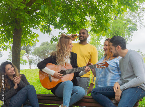 Group of interracial friends having fun and playing guitar in a park
