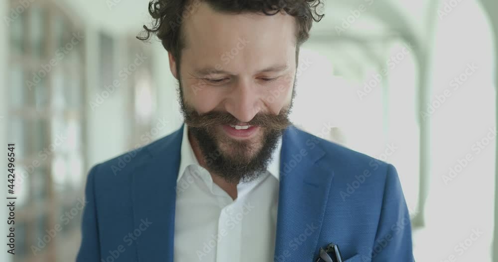 smiling curly hair man holding coffee, looking down at telephone, reading emails and messages and laughing when camera approaching outside smiling curly hair man holding coffee, looking down at telephone, reading emails and messages and laughing when camera approaching outside