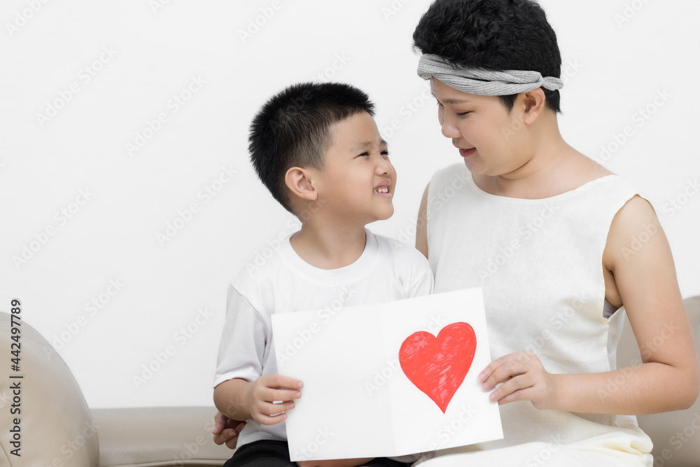 Cute Asian little boy son congratulating his mom happy with Mothers day, giving her handmade greeting postcard with red heart while sitting together on sofa at home. Family holidays concept Cute Asian little boy son congratulating his mom happy with Mothers day, giving her handmade greeting postcard with red heart while sitting together on sofa at home. Family holidays concept