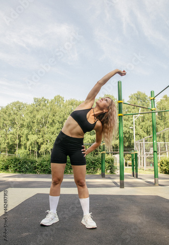 A blonde girl in a sports uniform, black leggings and a yellow crop-top, performs fitness exercises on the workout