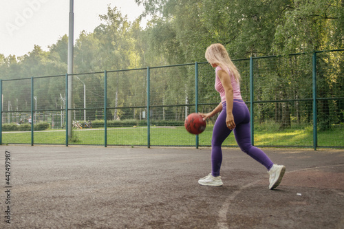 Blonde girl in sports uniform with a basketball on the playground