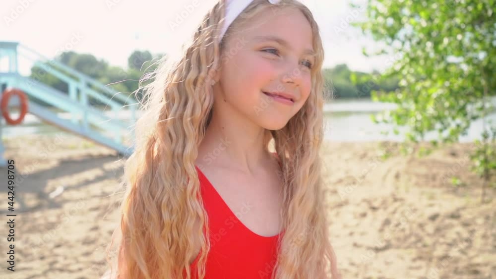 Young pretty blond girl in red bikini playing with her hair and dancing against blue lifeguard tower on the sand beach.